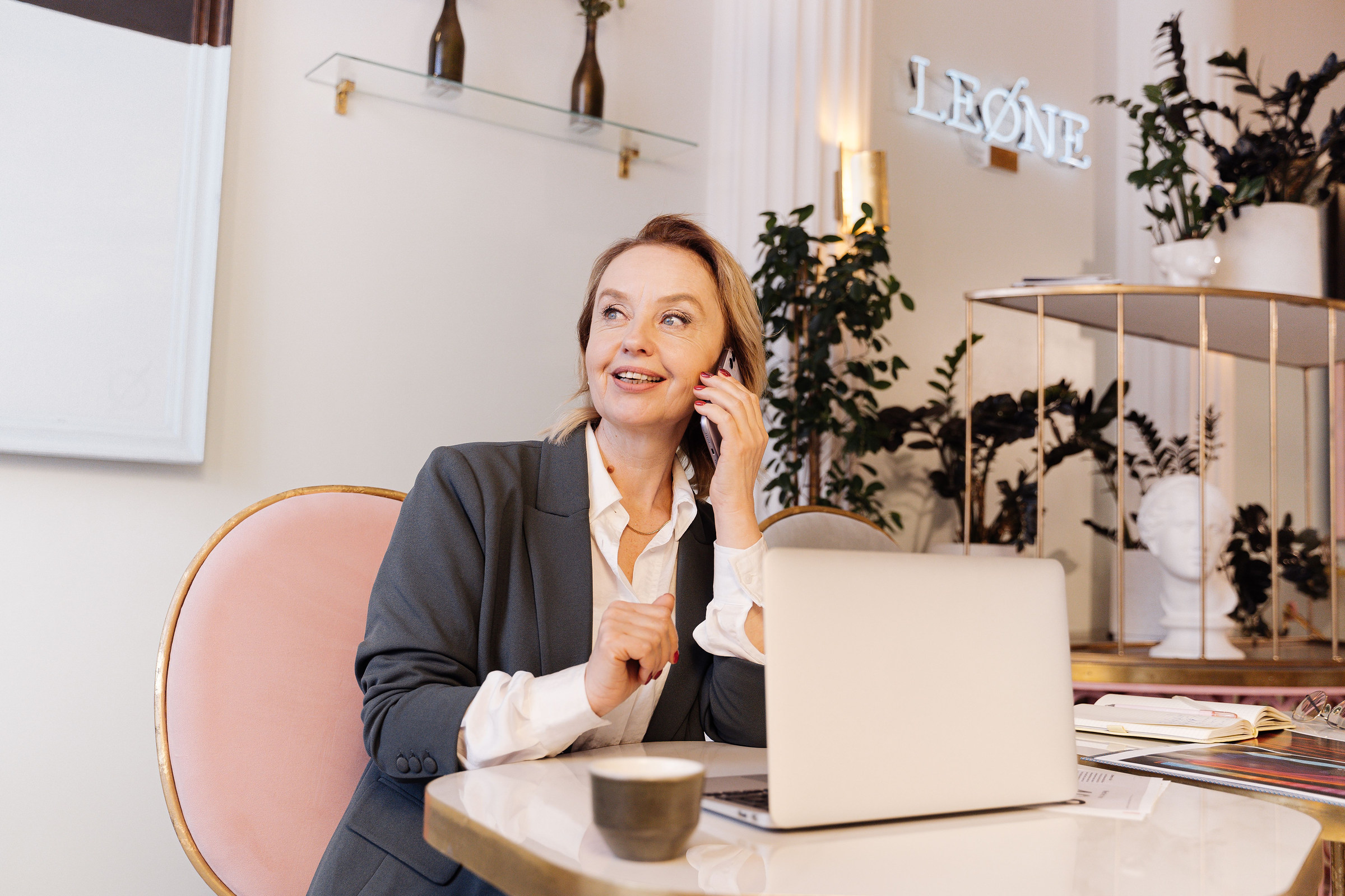 Smiling, polished business owner in a gray blazer answering a customer call at her desk in a bright, modern office