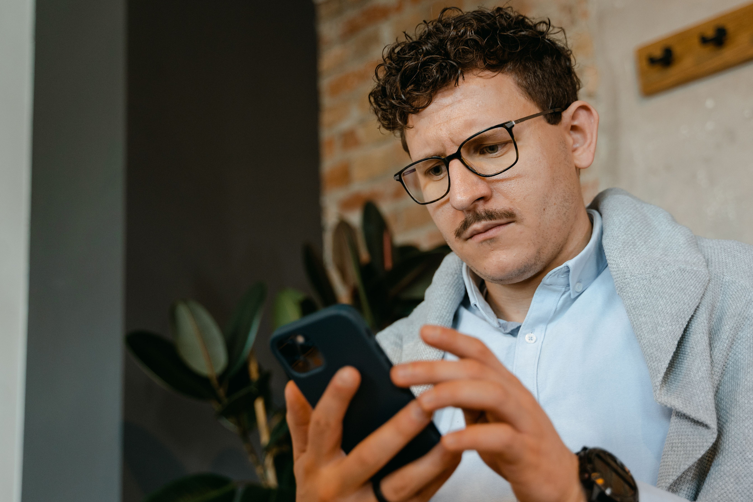 Business owner in glasses frowning at his phone as he reads an unfair one-star review on his Google listing