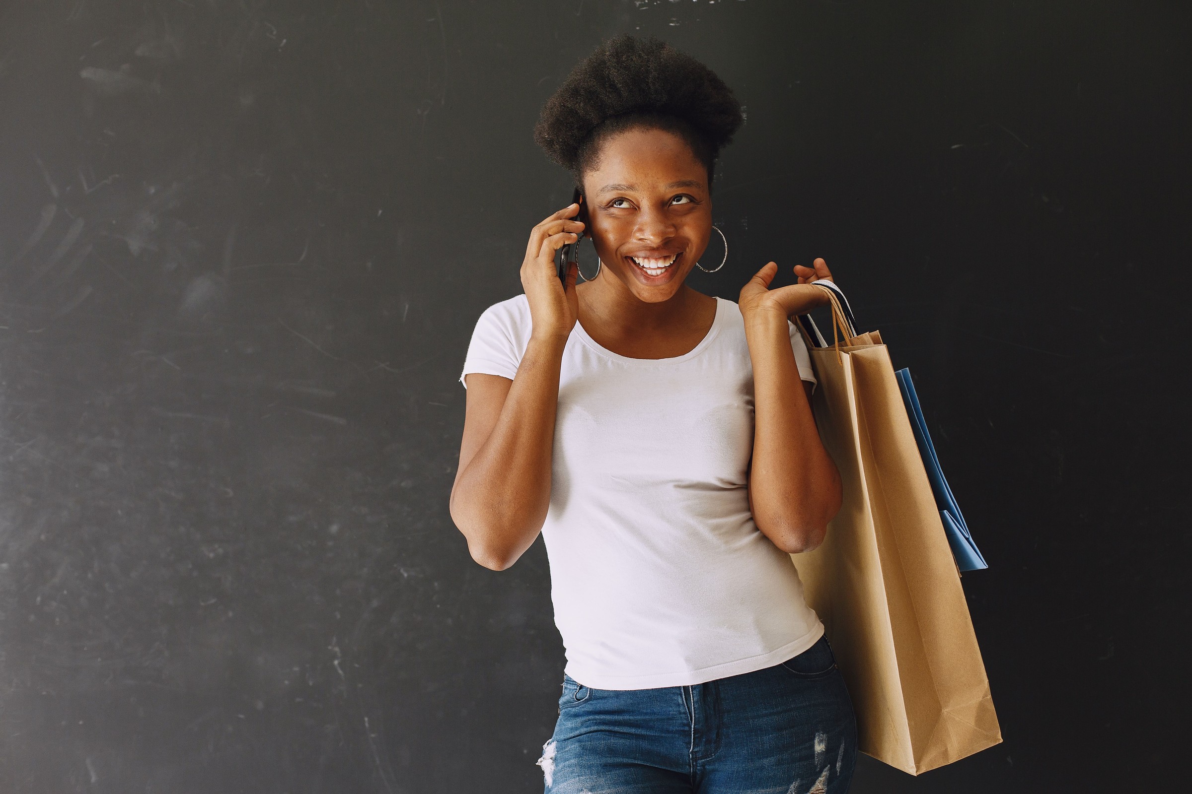 Smiling local business owner talking on a smartphone while carrying shopping bags, the kind of mobile brand-search moment when a Knowledge Panel or AI Overview is often the first thing a customer reads