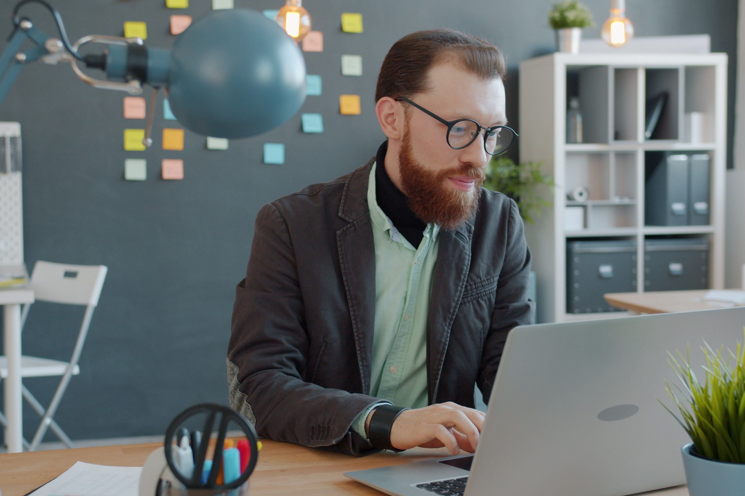 Bearded business owner in glasses working on his laptop in a bright office, reading a Google AI answer with links to local business websites