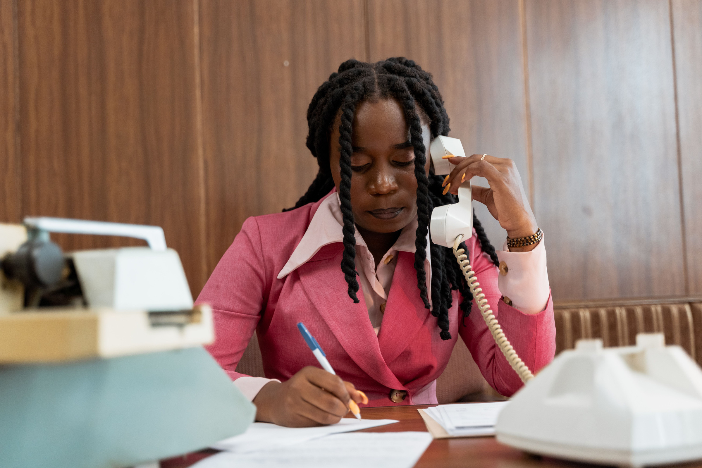 Front desk team member on a landline phone writing notes, asking a new caller how they heard about the business