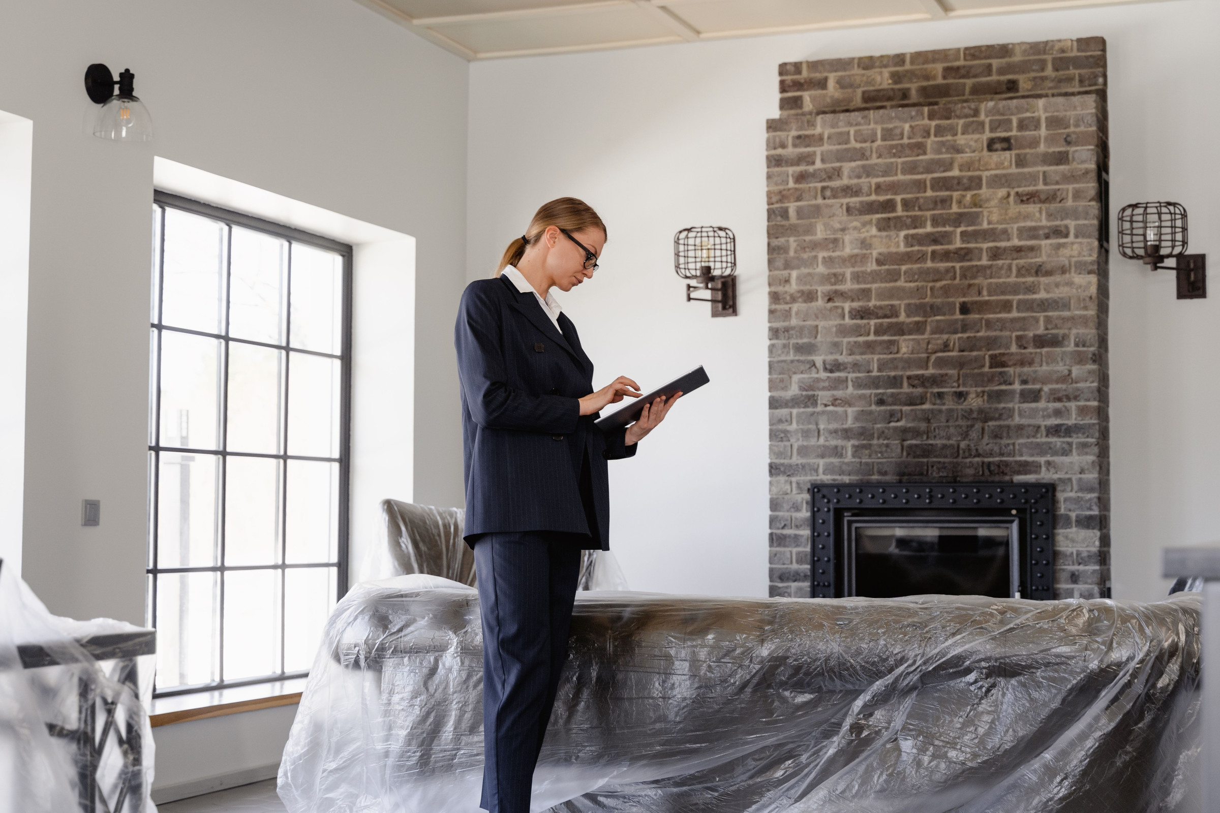 Home renovation pro in a dark suit standing in a house under renovation, checking her business website on a tablet between jobs
