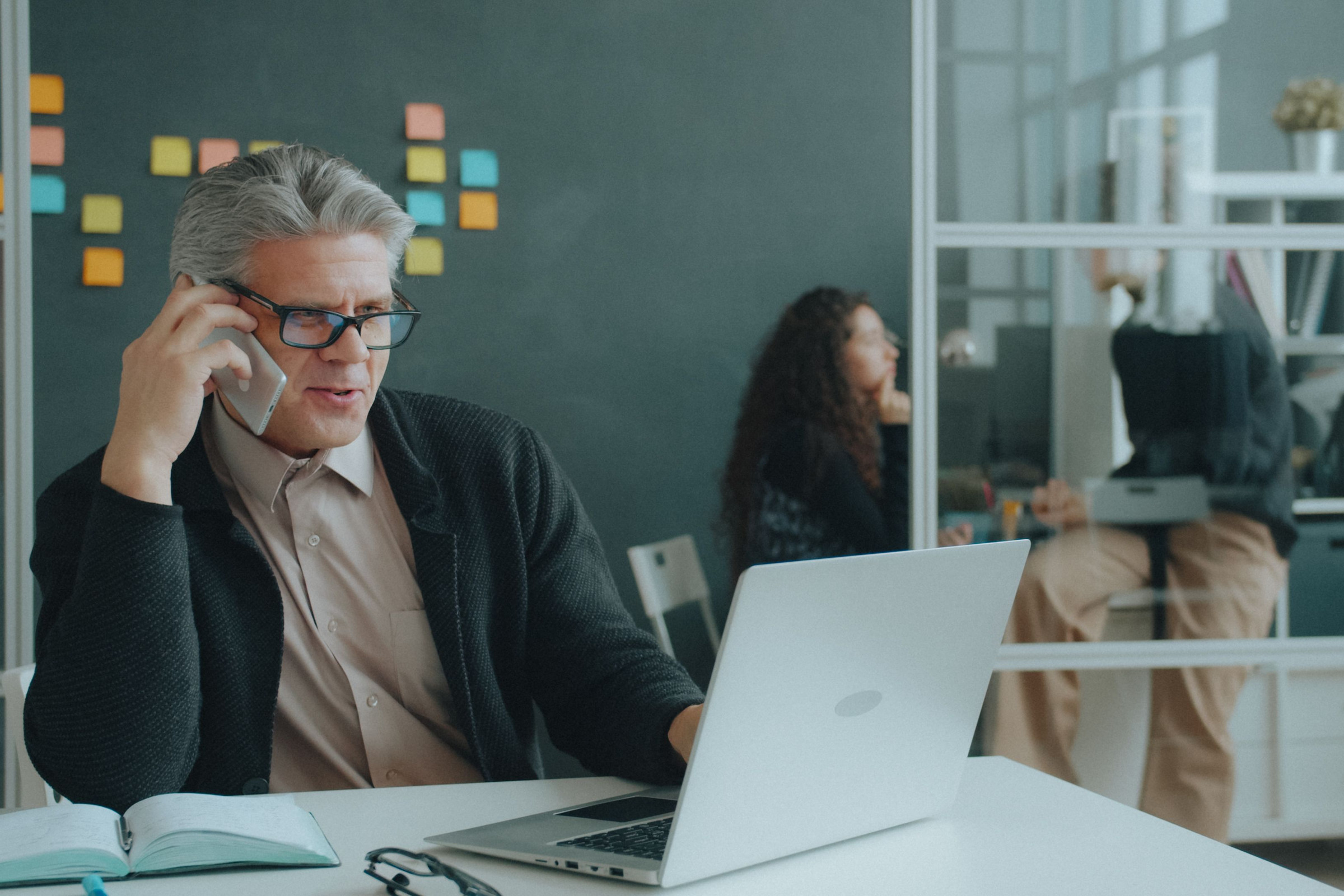 Business owner in glasses on a phone call at his office desk with a laptop open, talking with a new customer who filled out an ad form