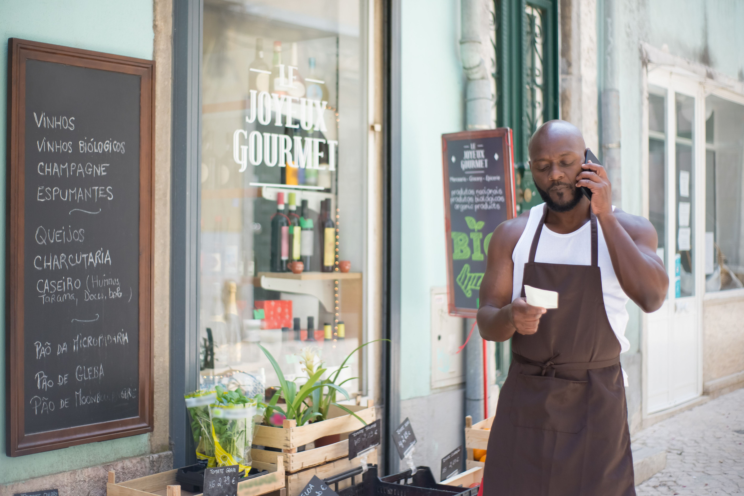 Shop owner in a brown apron standing outside his storefront taking a customer phone call, a sign that his phone is still ringing even when a report says otherwise
