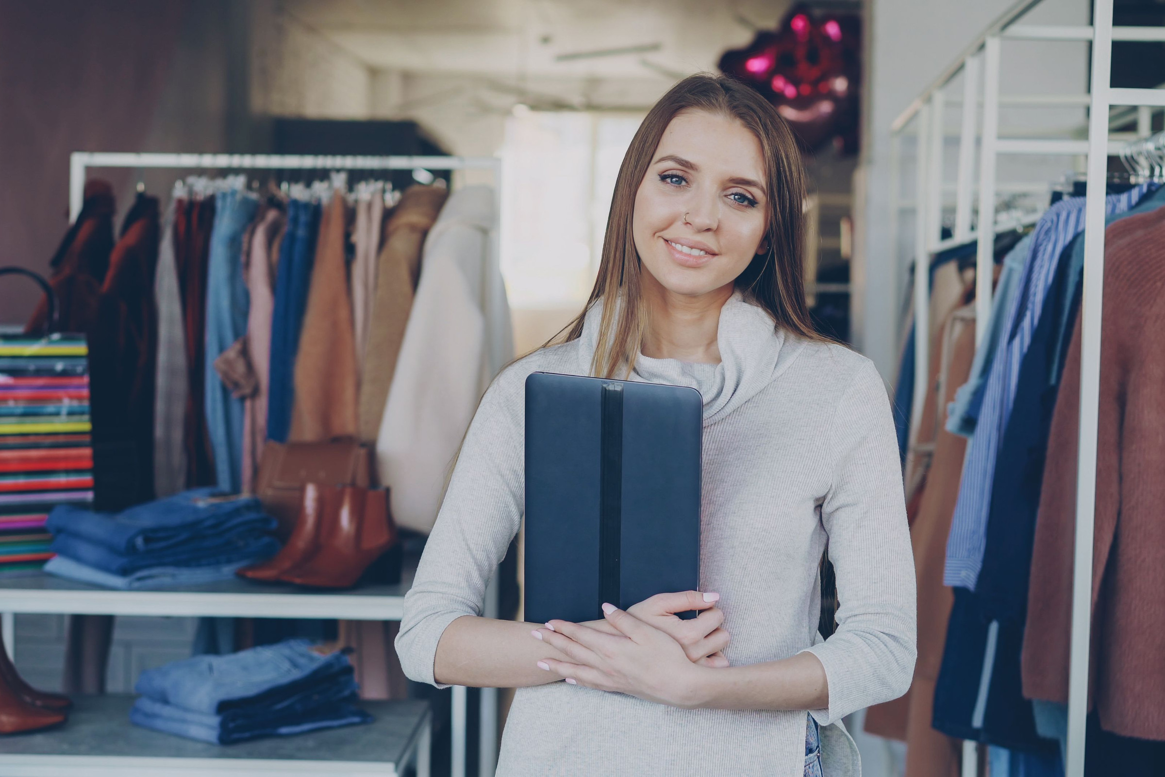 Smiling boutique owner holding a tablet between clothing racks in her shop, ready to update her store website