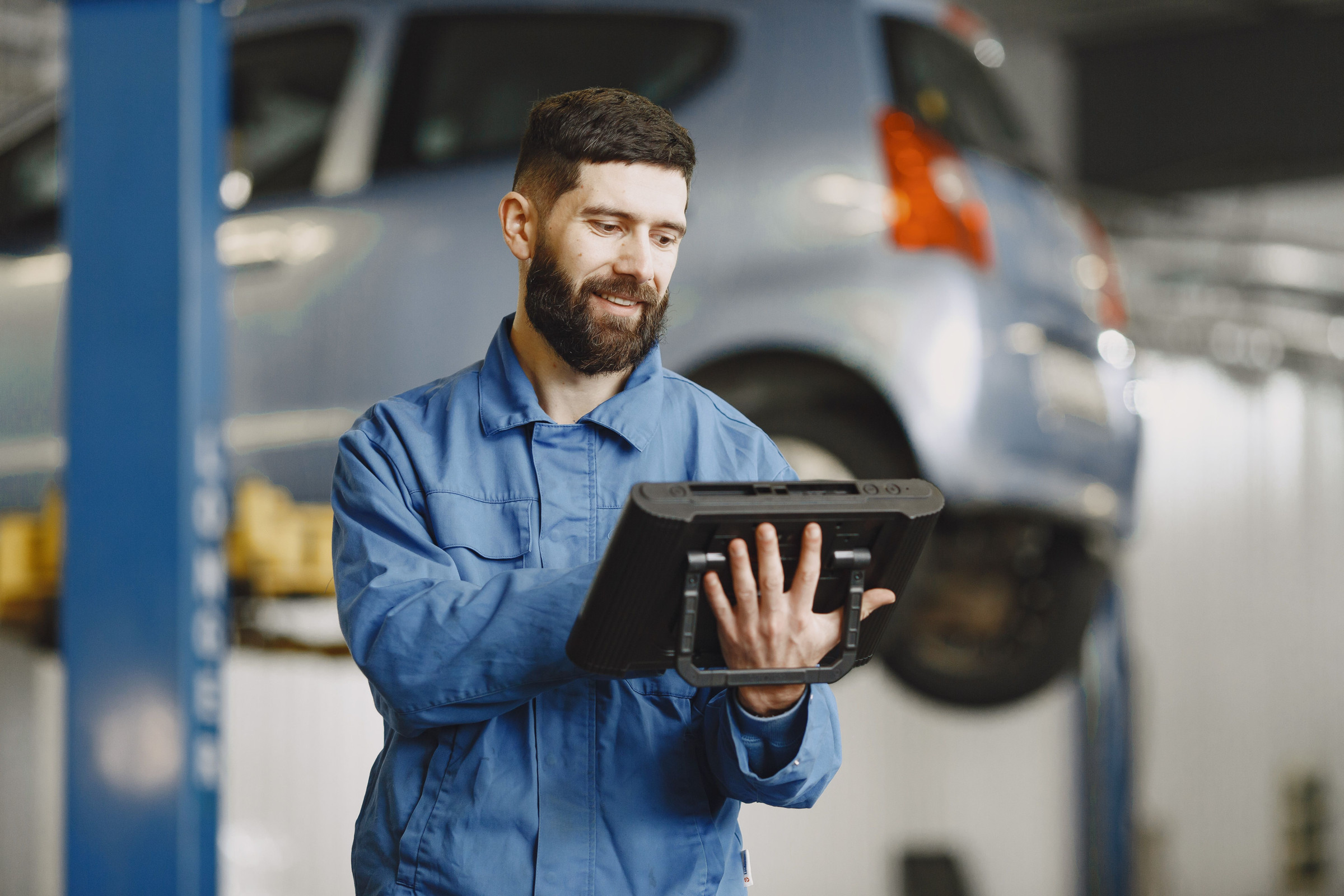 Auto shop owner in blue work clothes standing in his garage, checking his Google Business Profile calls and website clicks on a tablet