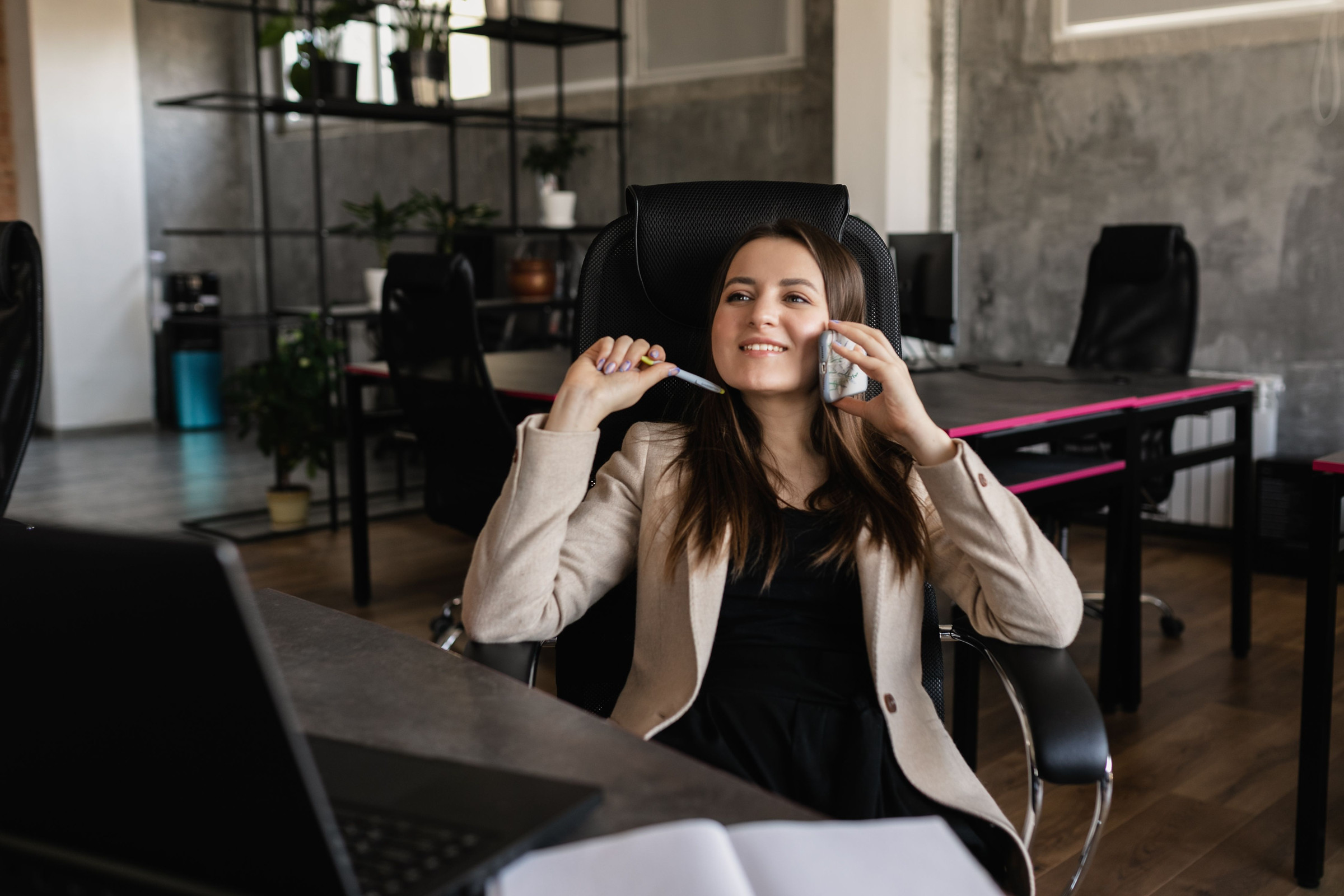 Smiling, polished business owner in a cream blazer taking a customer call at her desk in a modern office