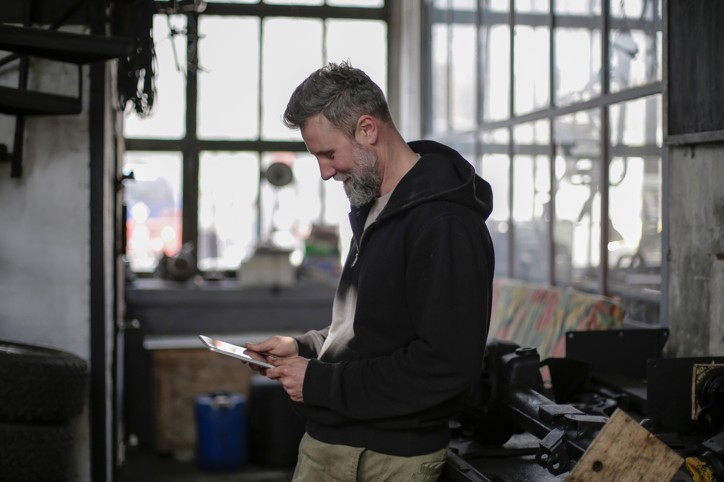 Workshop owner in a black hoodie standing in his shop checking Google Business Profile calls and website clicks on a tablet