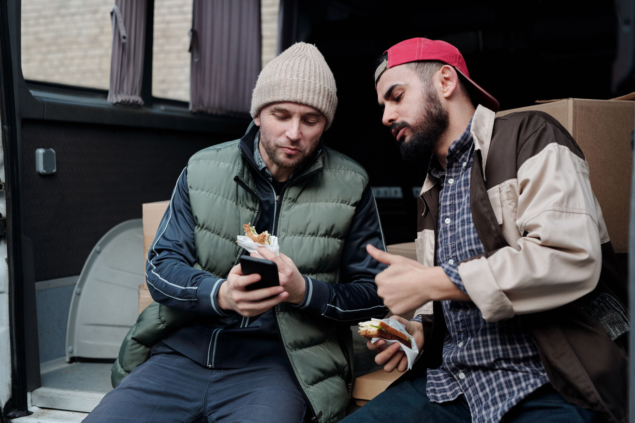 Two crew members on a lunch break in the back of their work van, looking at a phone together to check a new customer request