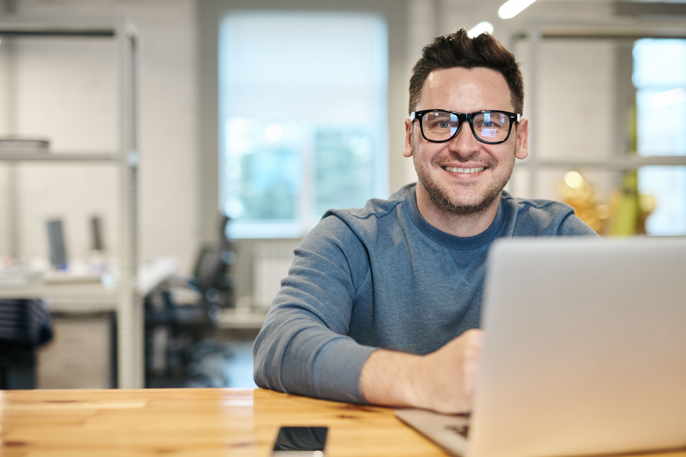 Smiling, friendly business owner in glasses checking his Google Business Profile on a laptop at a bright wooden desk