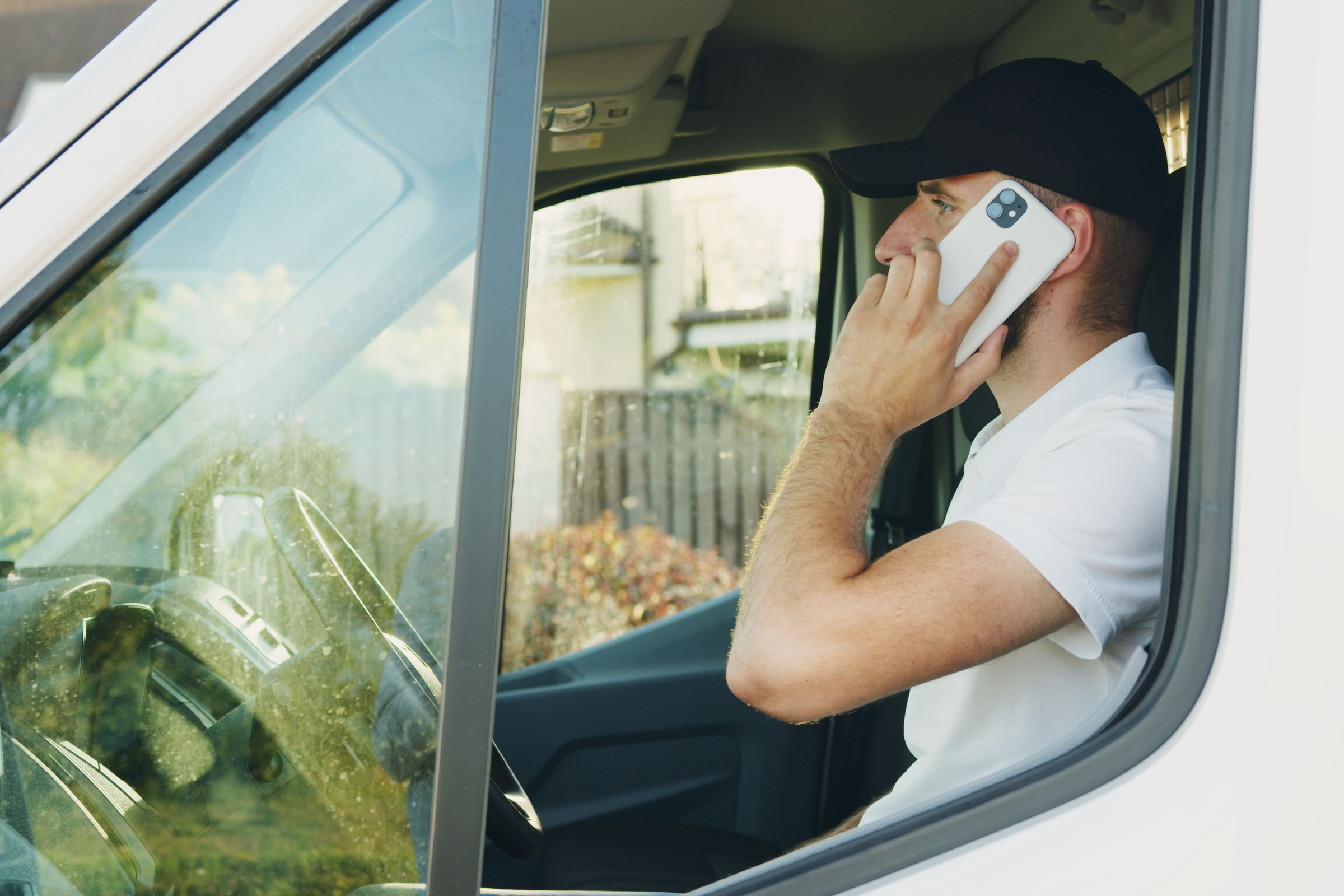 Service pro in a cap sitting in the driver seat of his white work van, calling a customer back between jobs