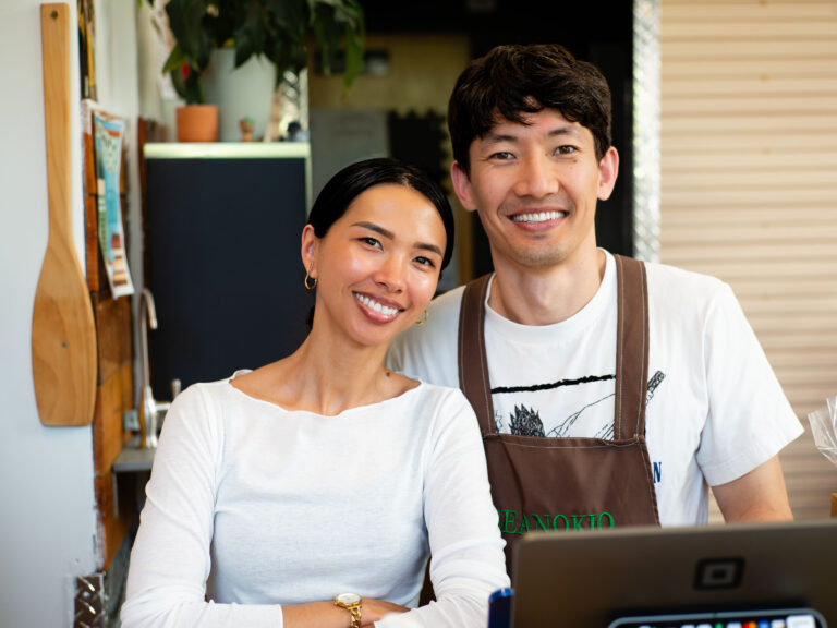 Two smiling, friendly café owners behind their counter with a laptop, ready to keep their Google Business Profile accurate