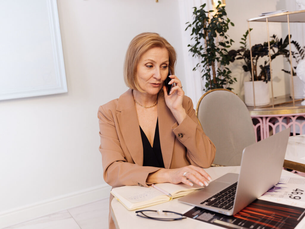 Local business owner in a tan blazer on a phone call at her desk with a laptop open, checking where new customer calls and website visits really come from