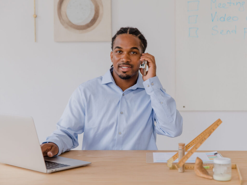 Smiling local business owner at a desk with a laptop and phone, ready to take calls from Google camera search visitors