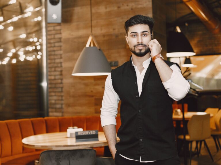 Restaurant owner in a black vest standing in his dining room on a phone call, making sure the call button on his Google Business Profile reaches a real person