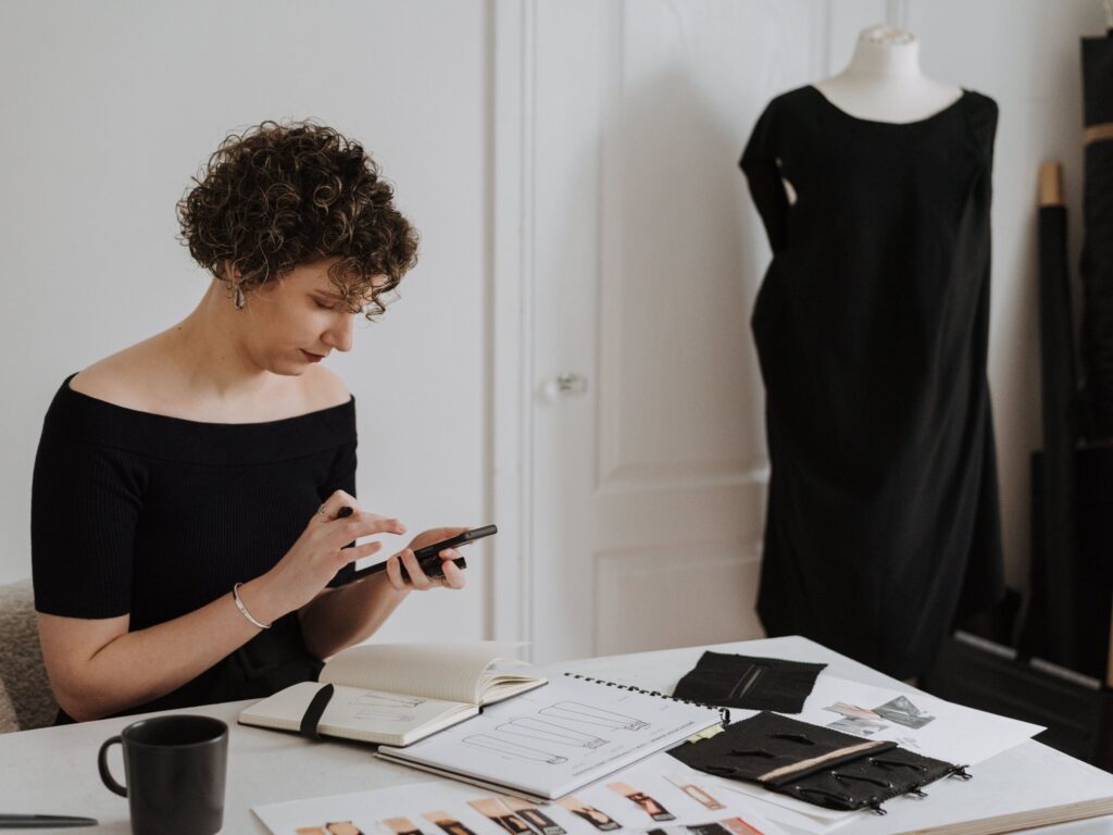 Small business owner checking customer messages on her smartphone at her studio desk, illustrating Google's AI agent answering customers on Business Profiles